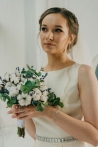 A bride holding a cotton and eucalyptus bouquet, showcasing elegance and style indoors.
