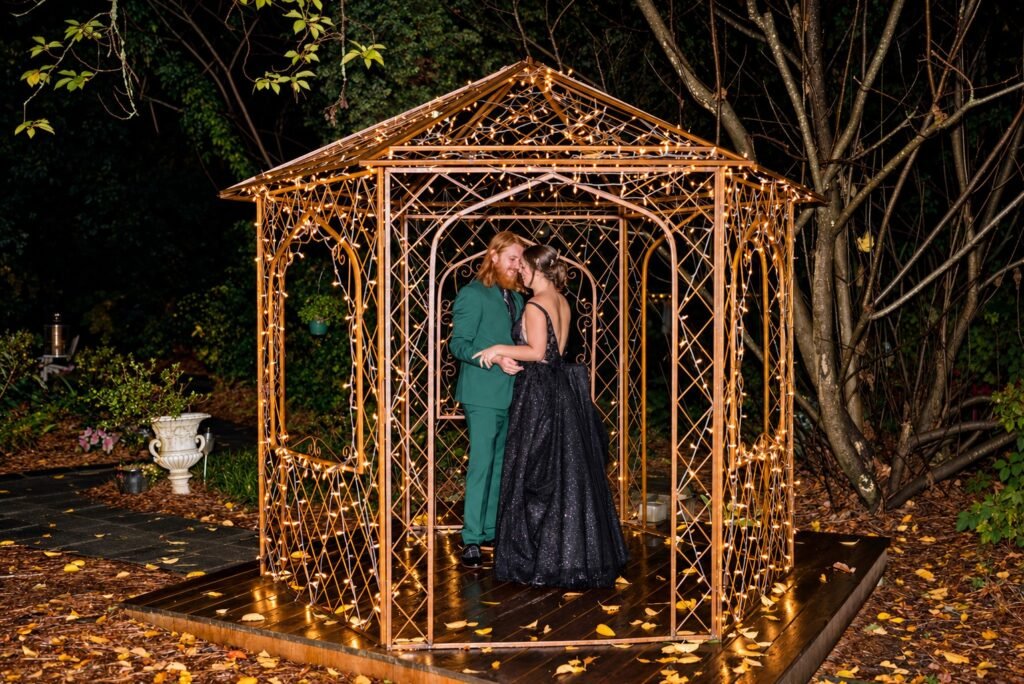 Parker and Olivia embracing under an illuminated garden gazebo at night at Four Oaks Manor
