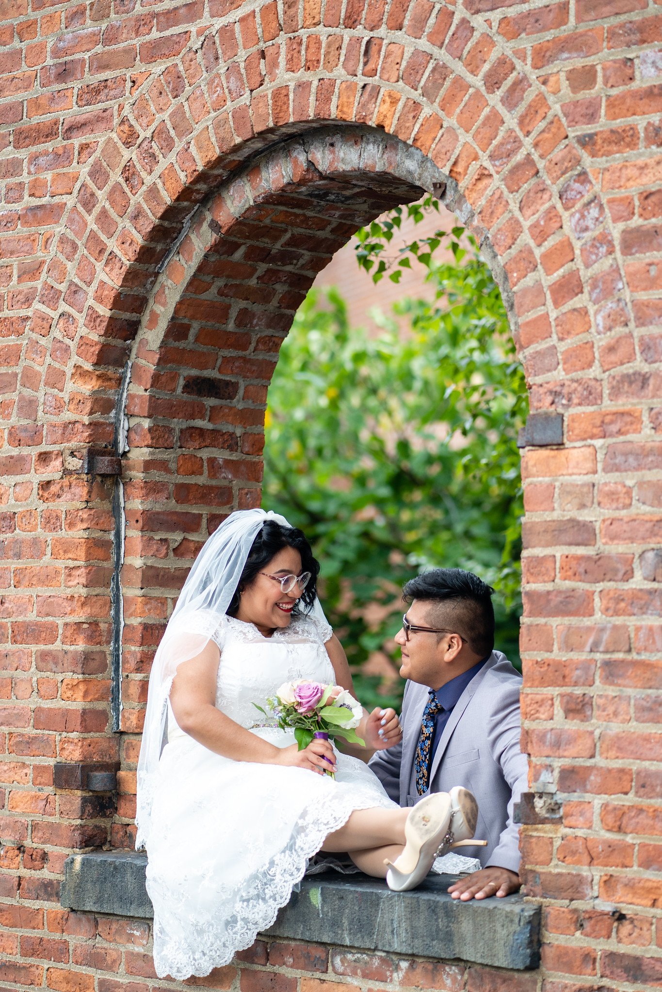 Brenda and David sit together in a brick window opening.