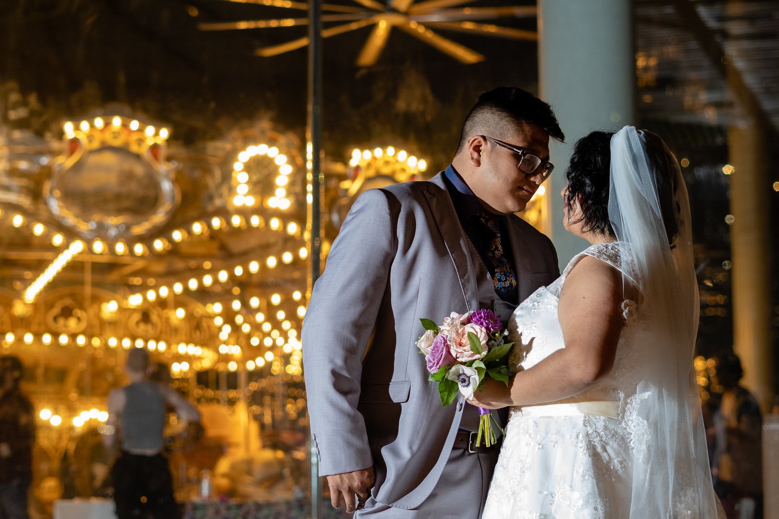 Brenda and David look at one another in front of glowing carousel lights.