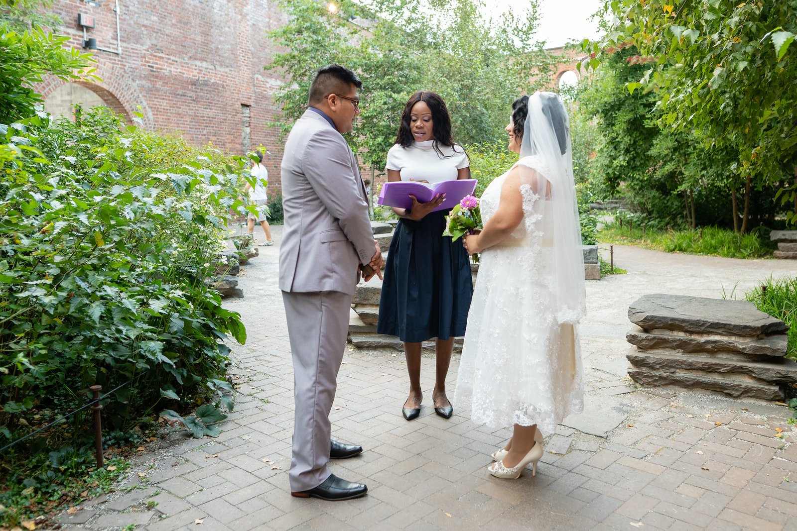 Brenda and David stand with their officiant during a garden ceremony.