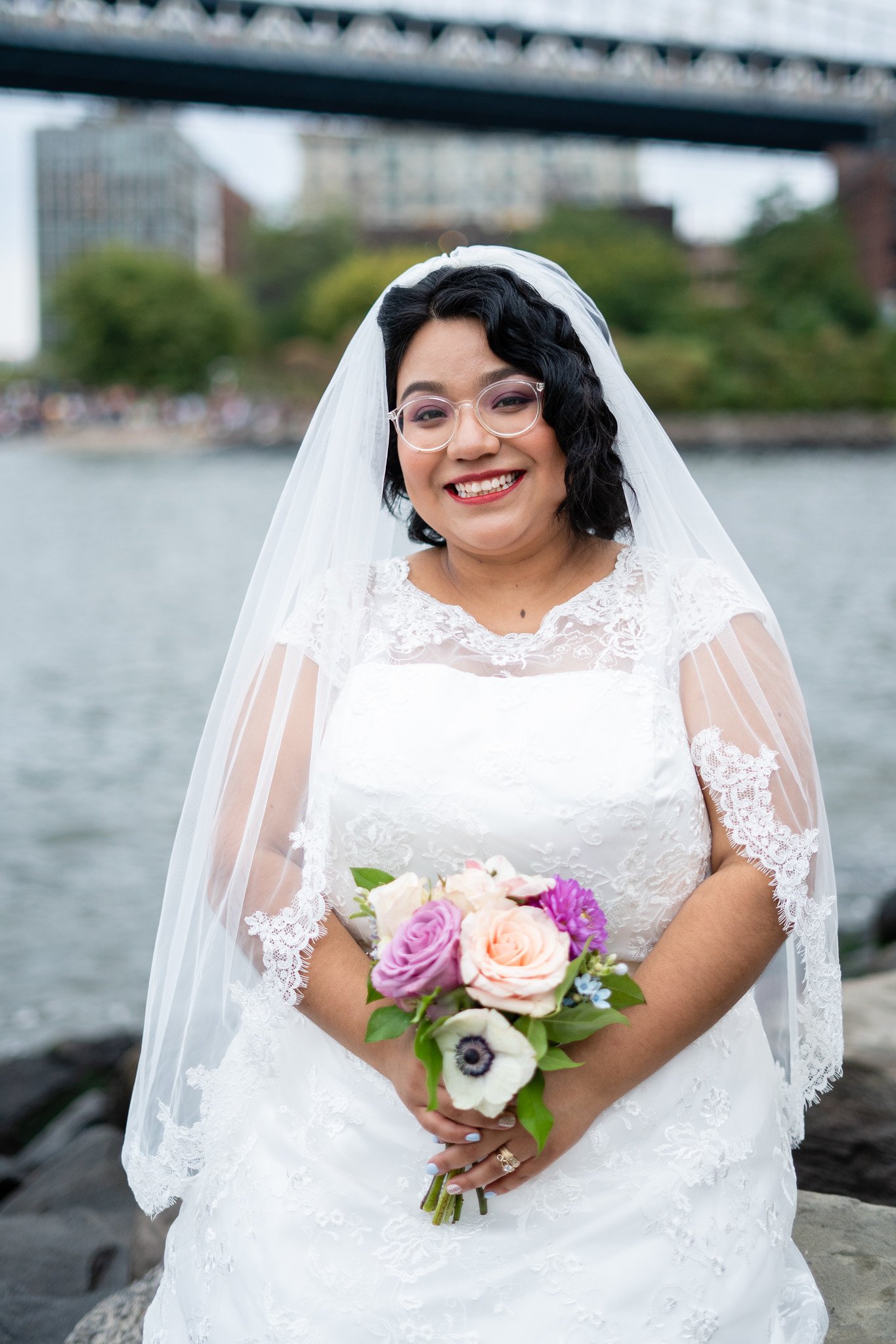 Brenda smiles with her bouquet beside the water.