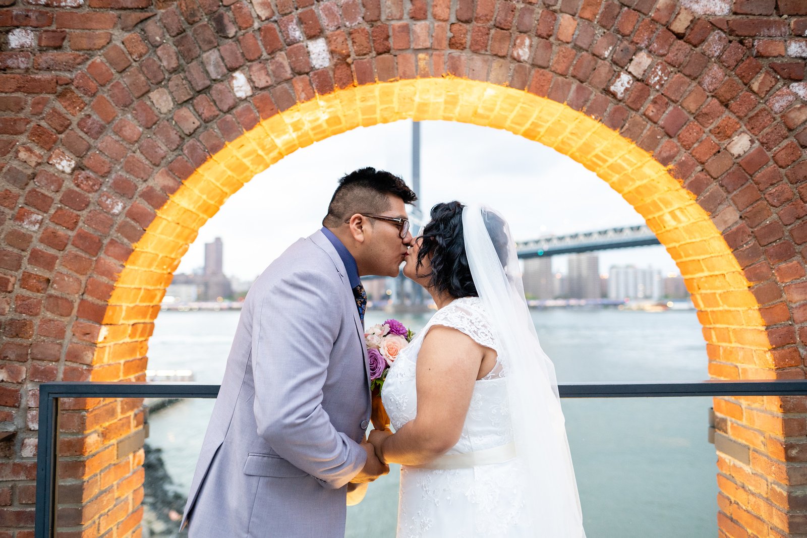 Brenda and David kiss beneath a warmly illuminated brick arch.