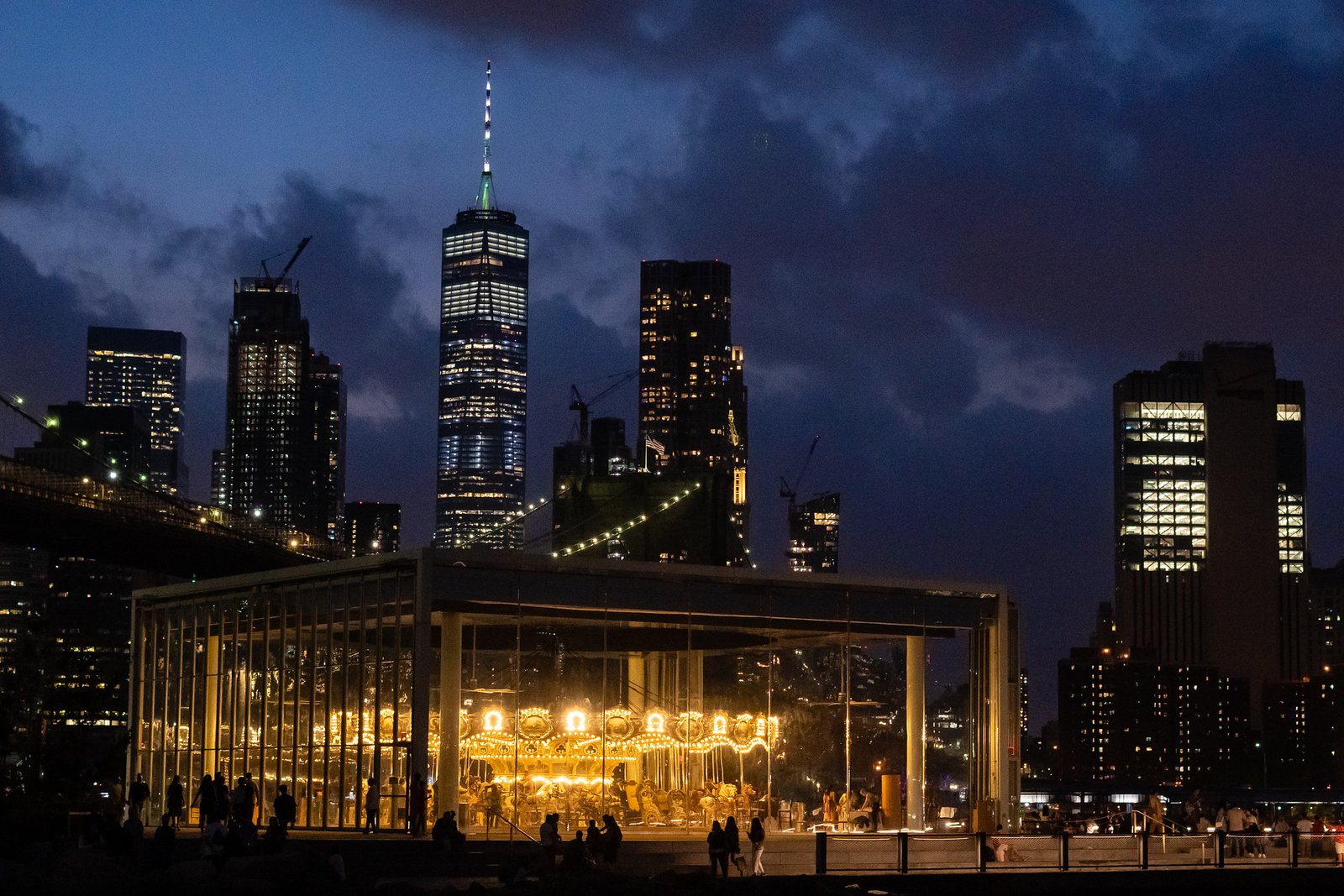 An illuminated carousel beside the water beneath the night skyline.