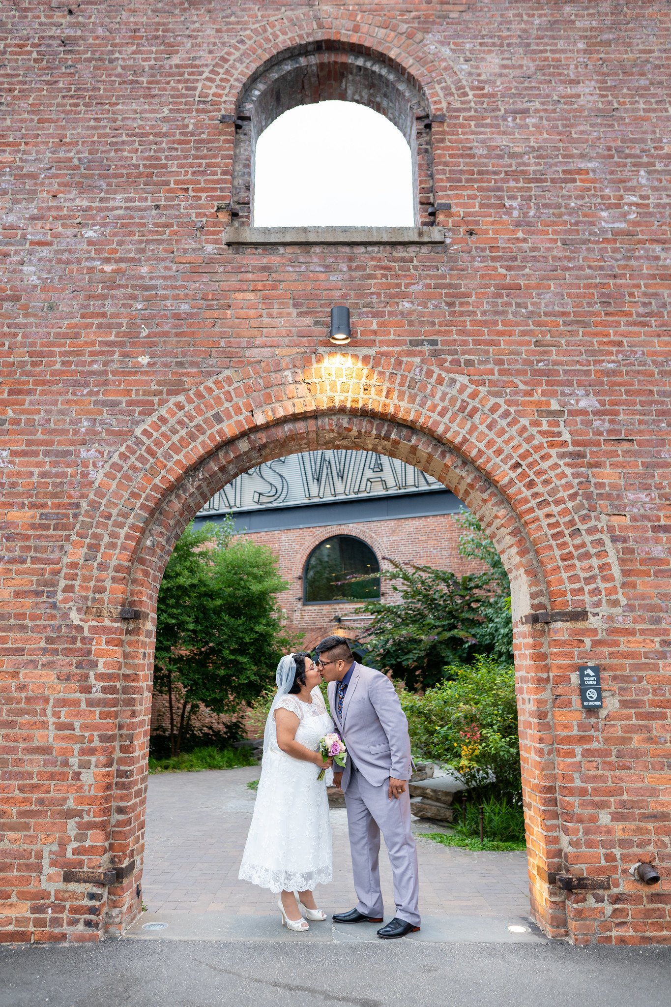The couple kiss beneath a tall brick arch.
