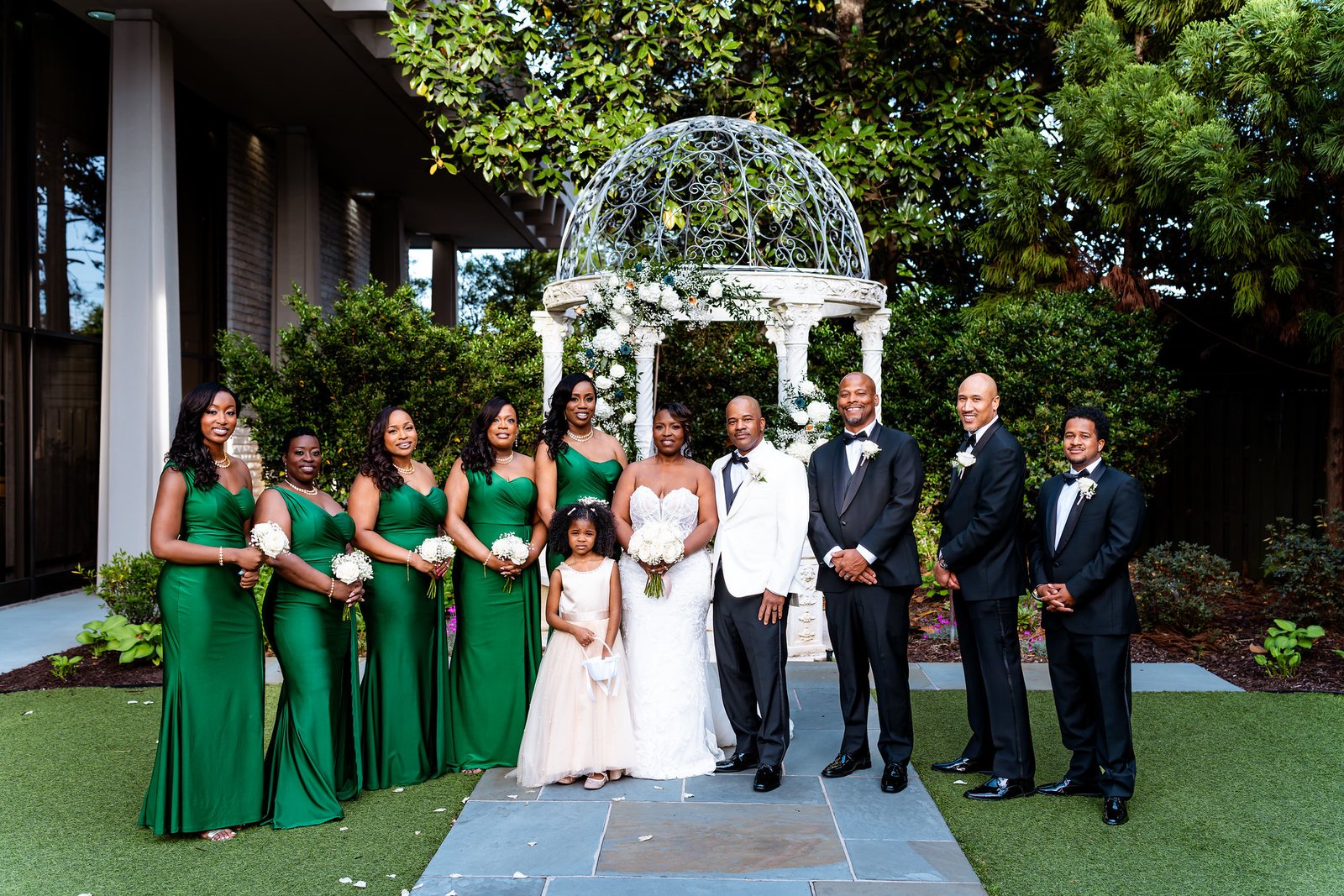 The couple and wedding party standing together beneath the garden gazebo.