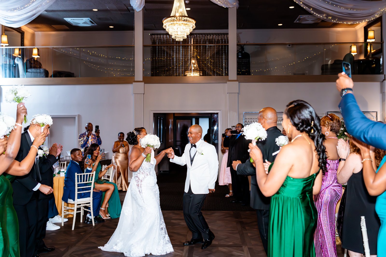 The newlyweds enter the reception holding hands as guests cheer around them.