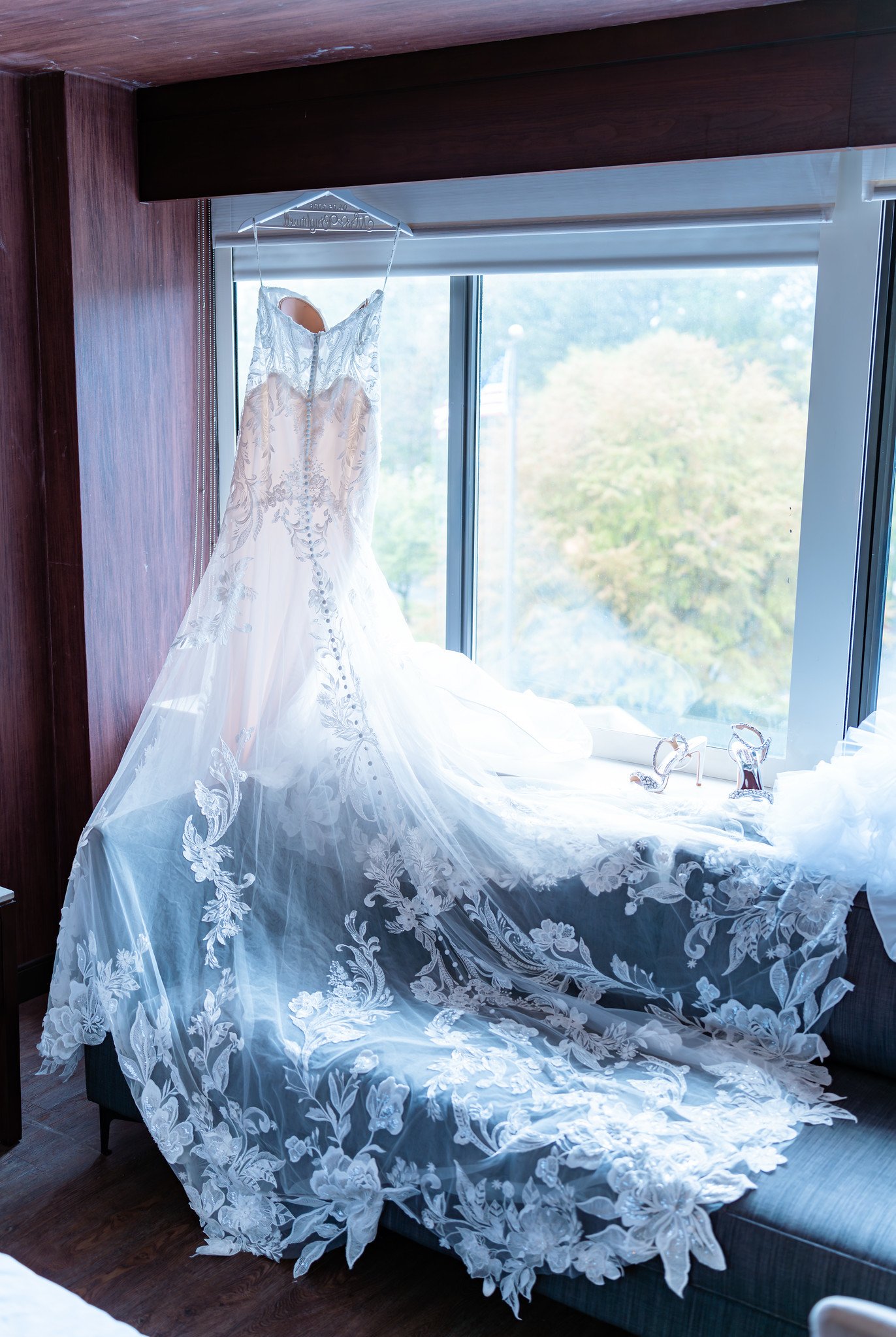 A wedding dress and sparkling heels arranged by a window.