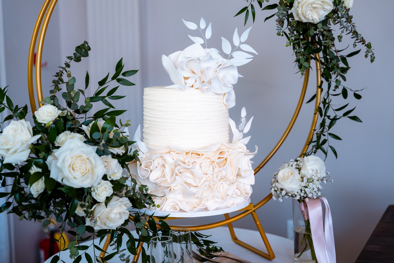 A white wedding cake framed by flowers and a gold circular stand.