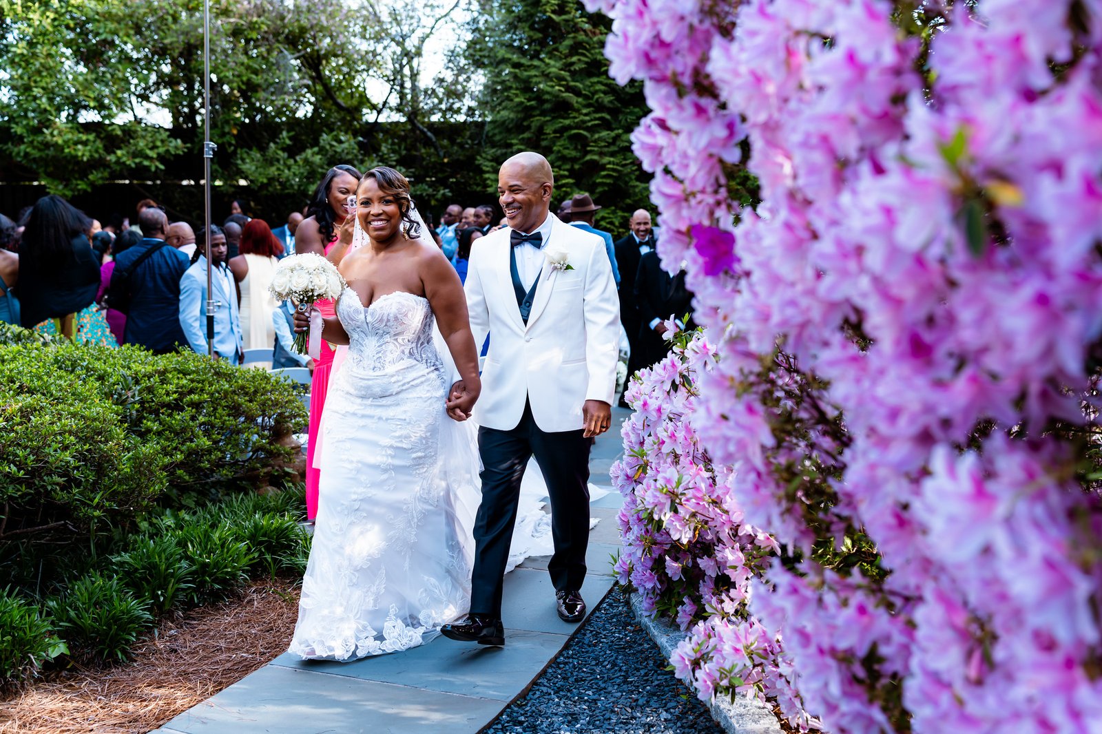 The newlyweds walking hand in hand beside blooming pink flowers.