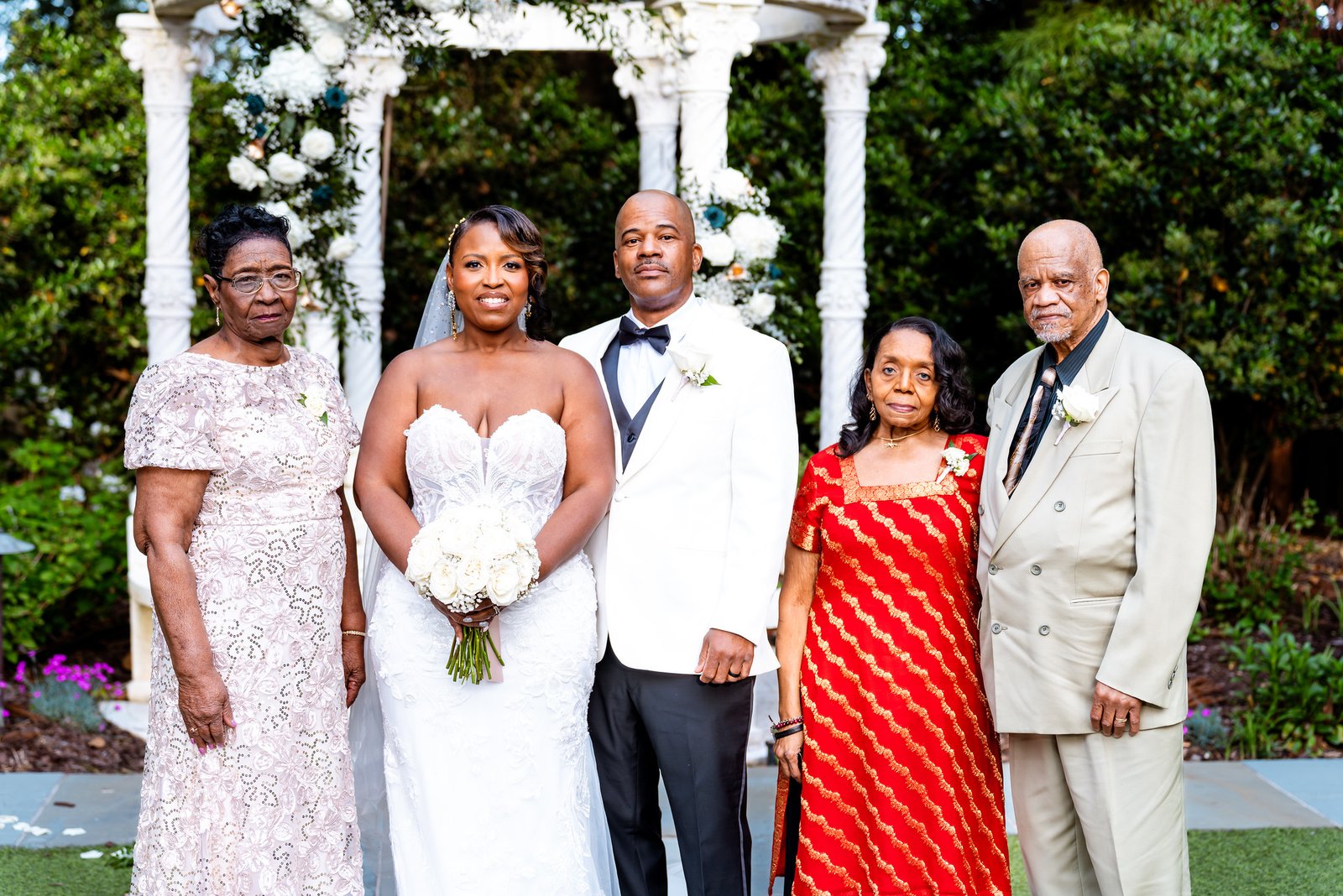 The newlyweds standing with three guests near the garden gazebo.