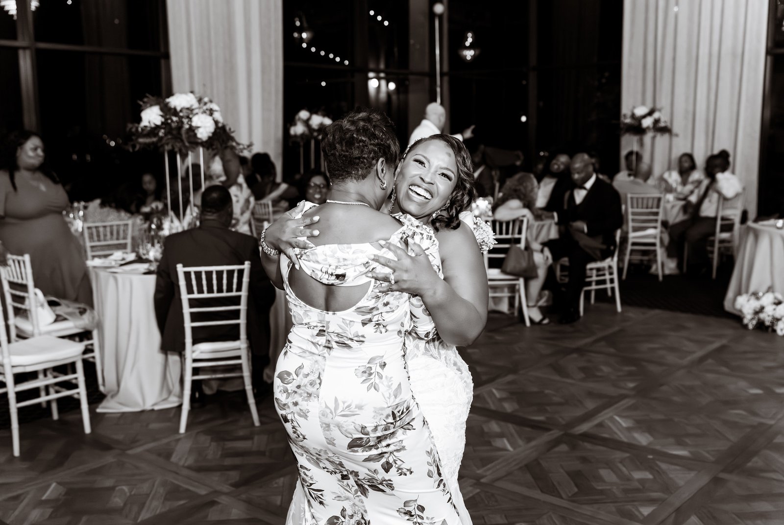 The bride smiles broadly while embracing a guest in a black-and-white photograph.