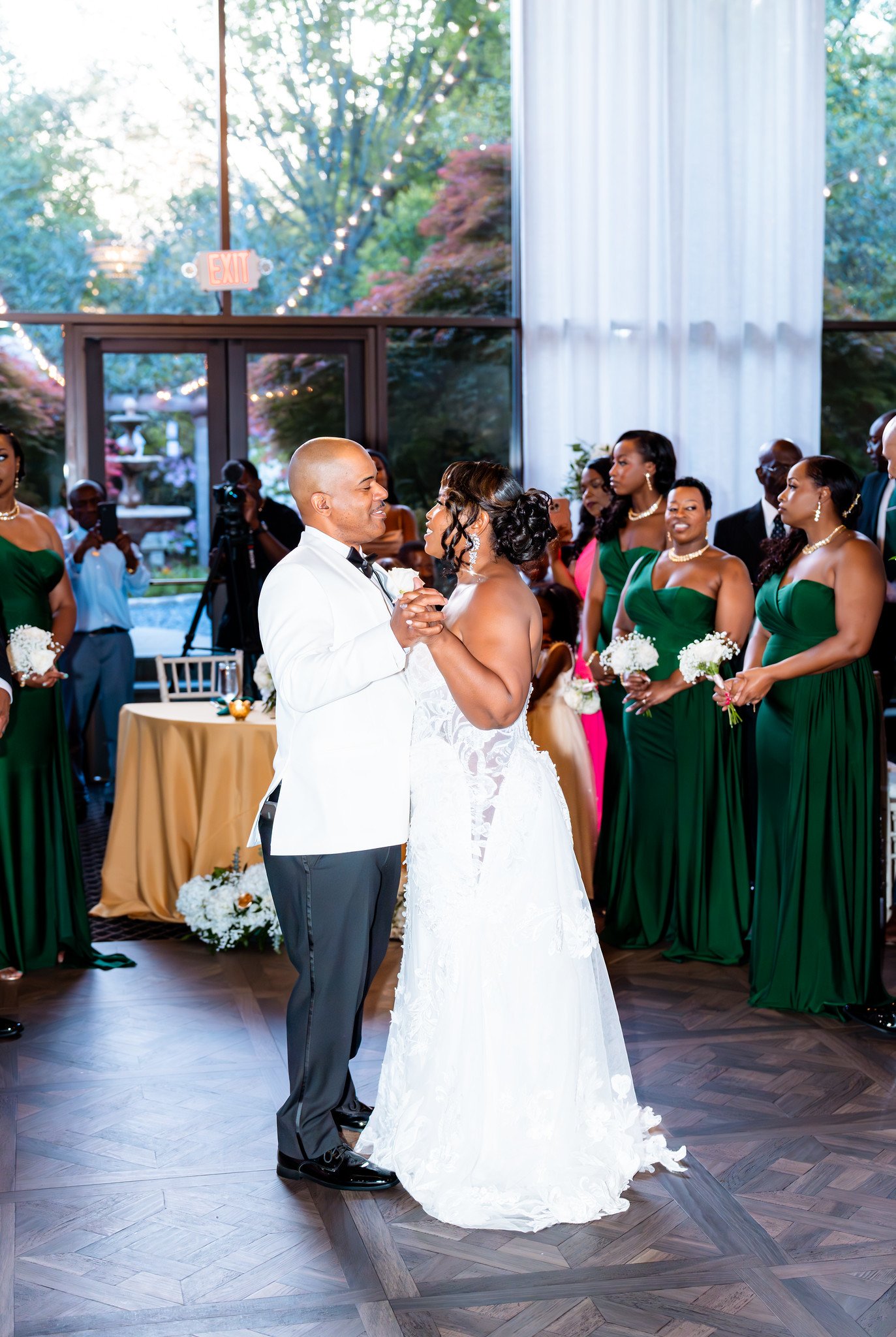 The bride and groom share a dance in front of the reception’s tall windows.