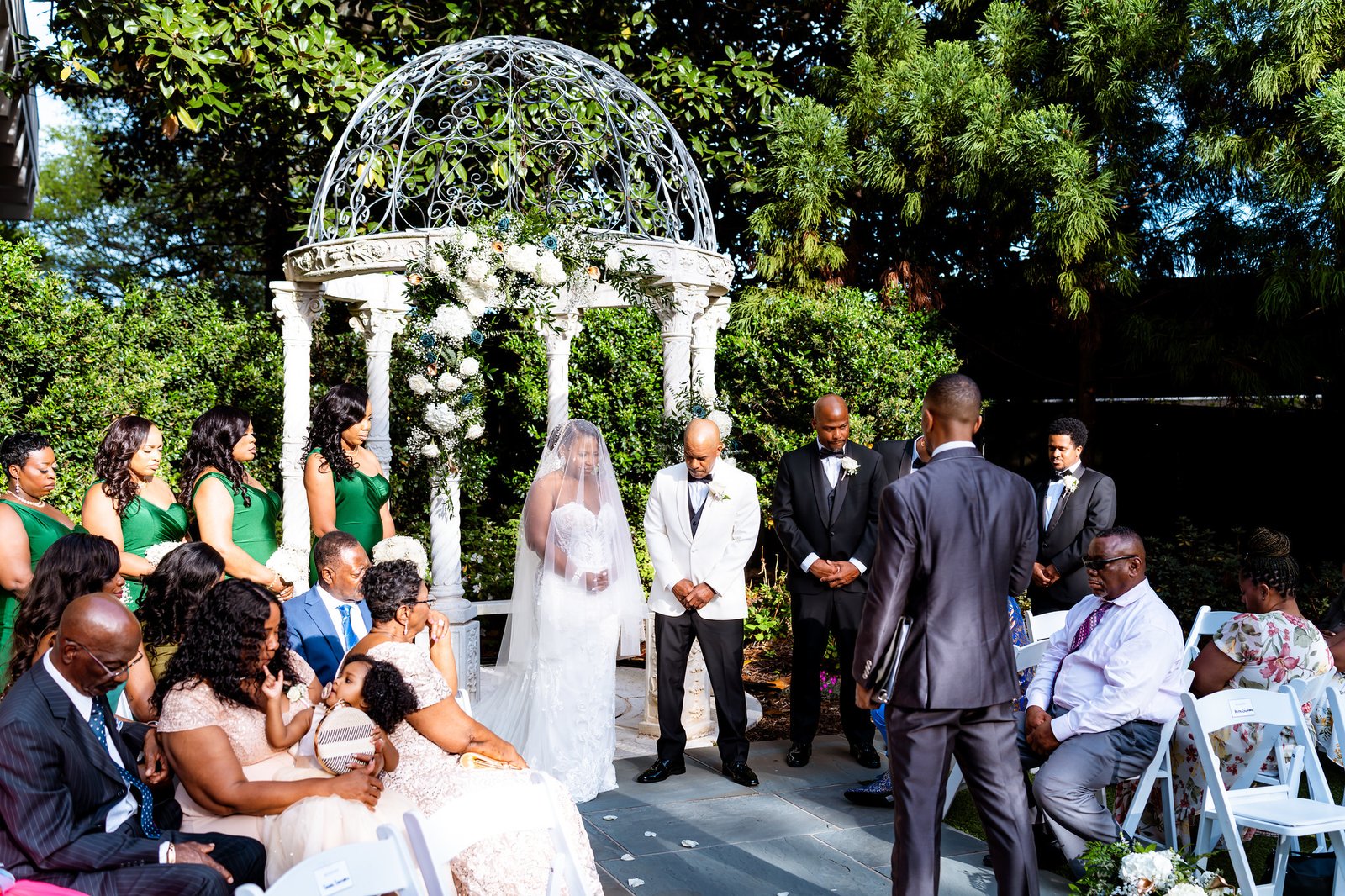 The couple standing beneath a flower-decorated gazebo during their garden ceremony.