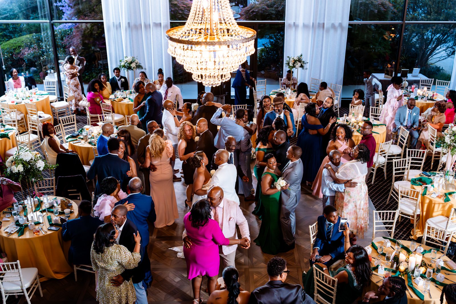 An elevated view shows couples dancing beneath a chandelier among gold-covered reception tables.