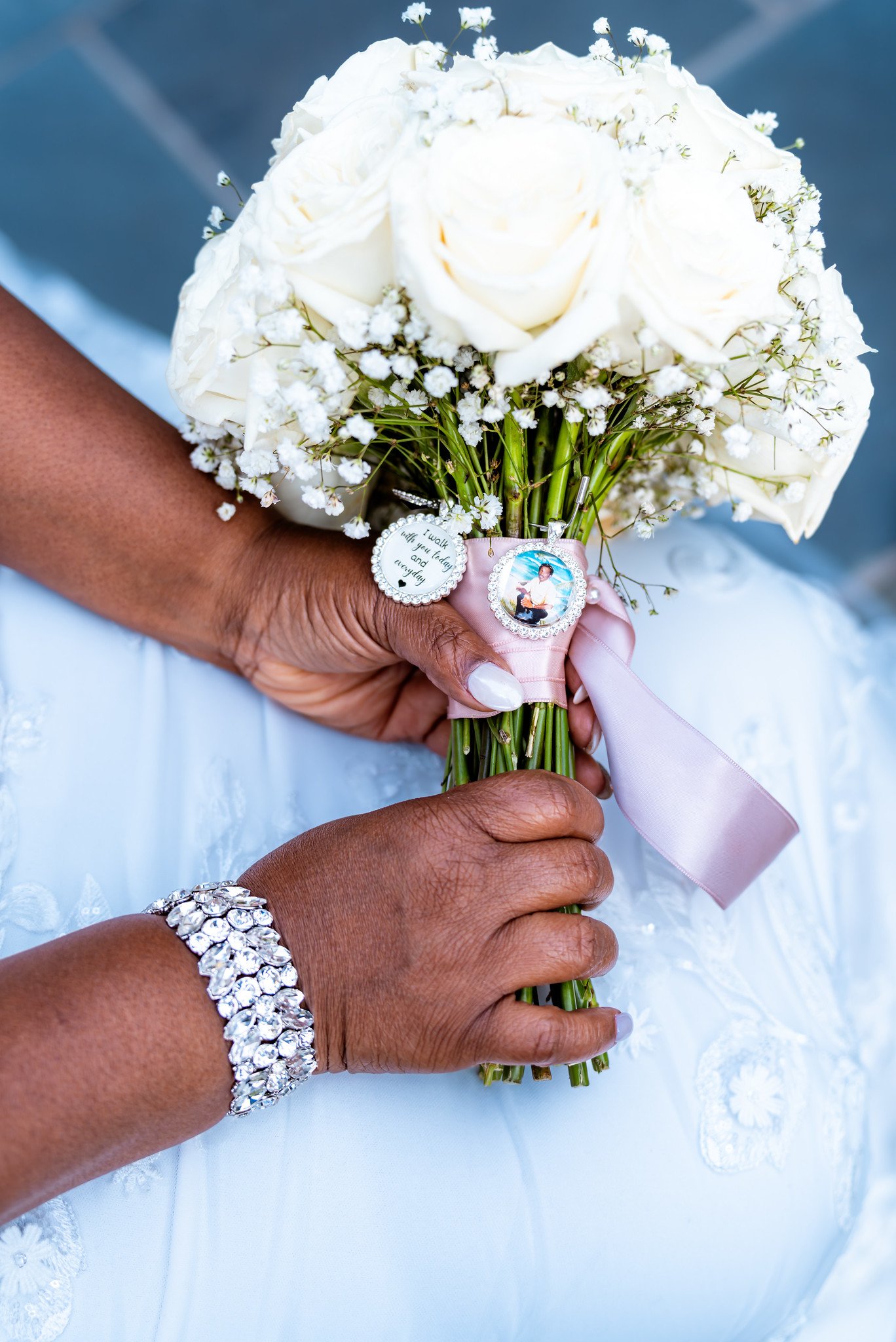 The bride holds a white rose bouquet with a pink ribbon and a photograph charm.