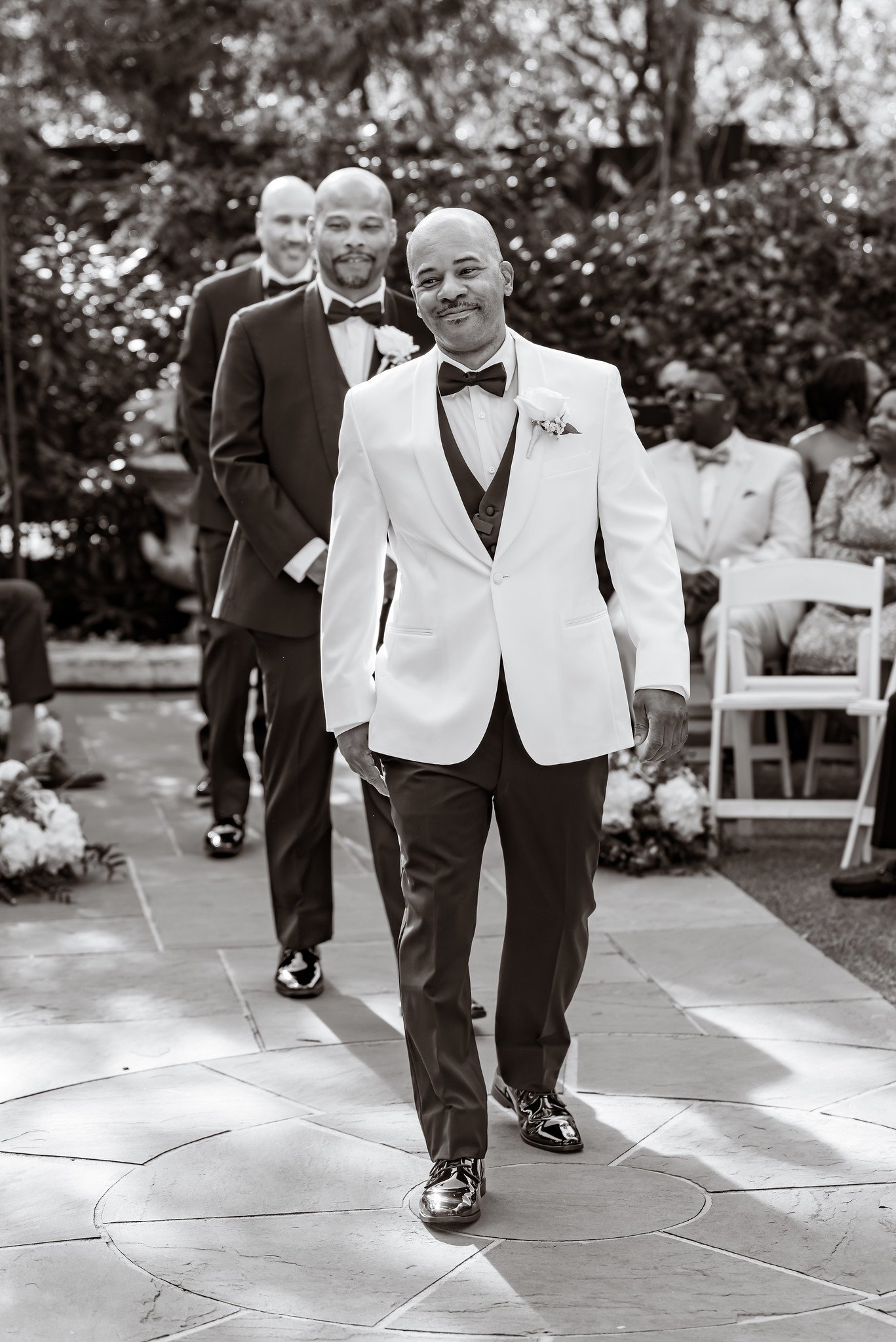 The groom walking toward the wedding ceremony with his wedding party behind him.