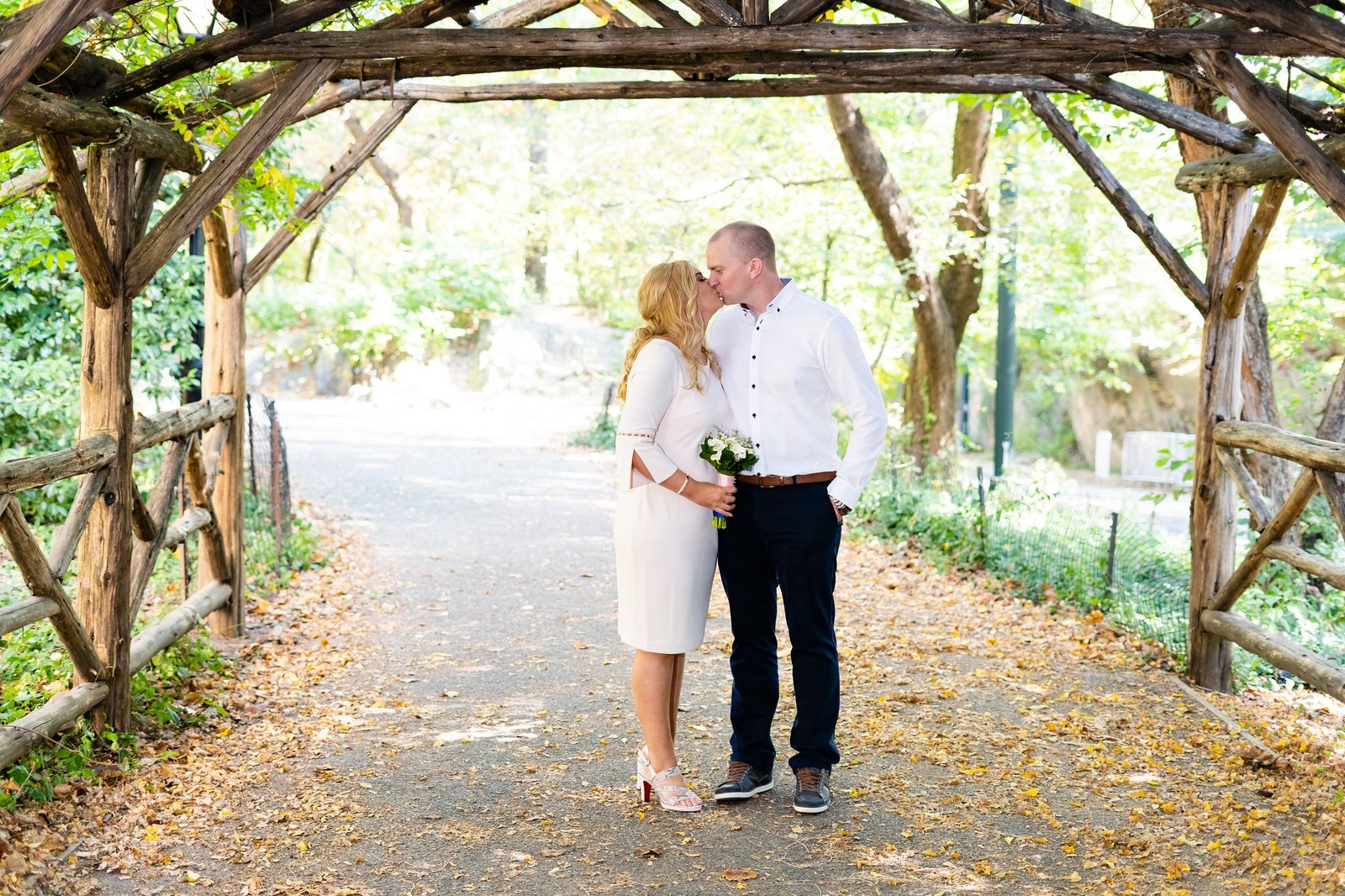 Mary and Shamus kiss beneath a rustic wooden arch.