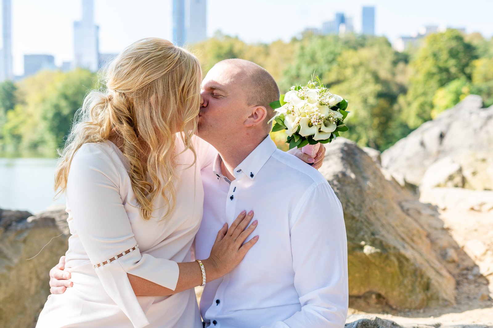 A close kiss with the water and trees behind the couple.