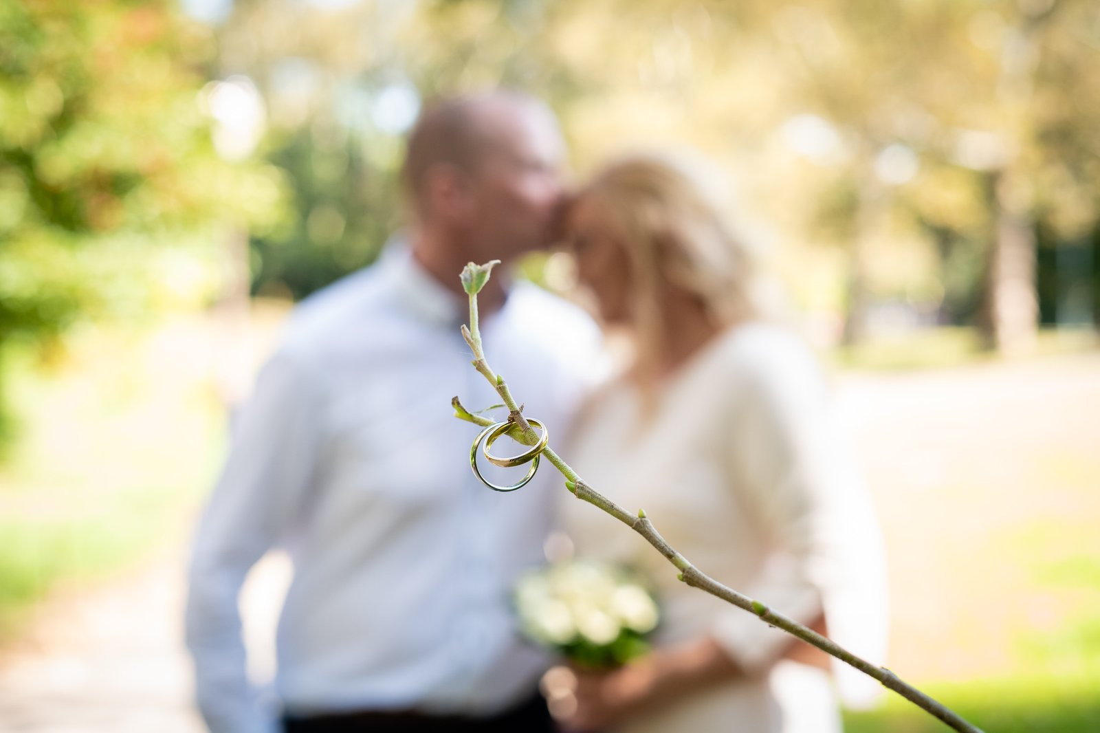 Wedding rings in focus with the couple kissing softly in the background.