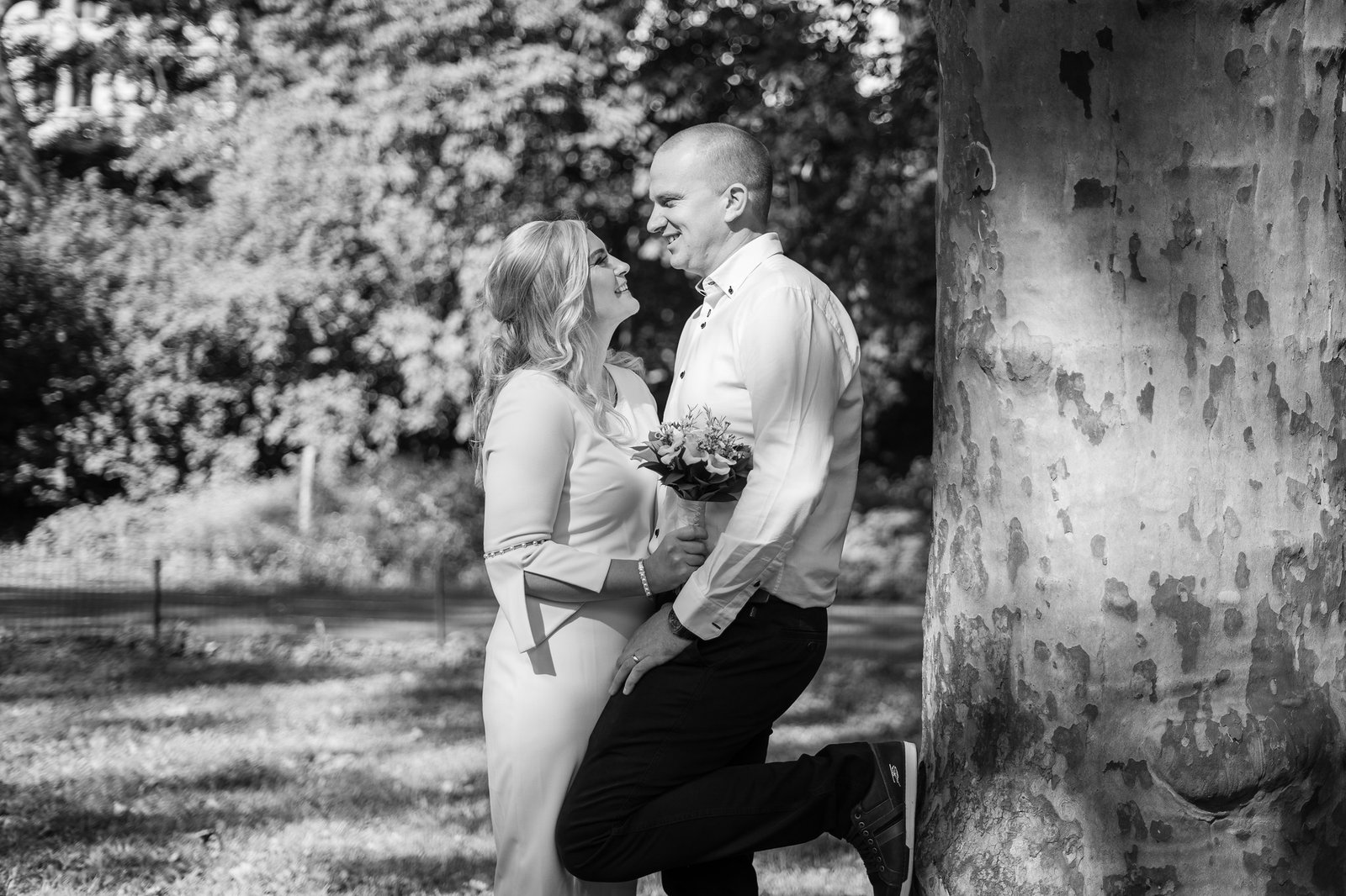 Mary and Shamus smile toward one another beside a tree in black and white.