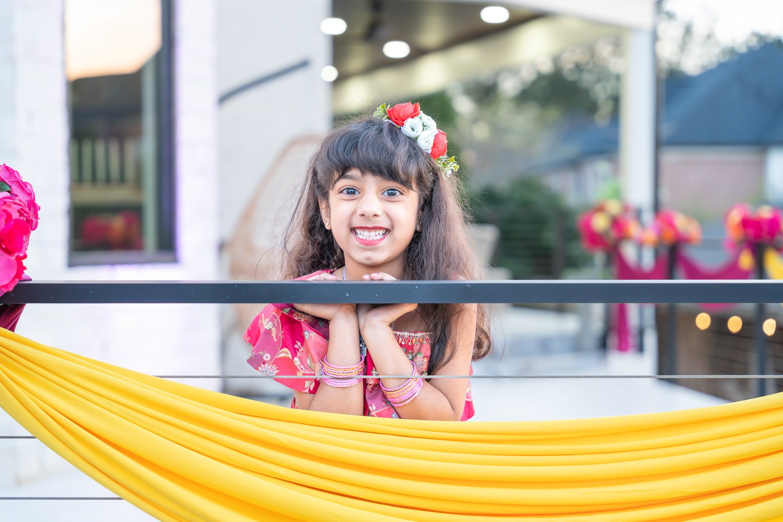Young guest smiles over a railing decorated with yellow fabric and flowers.