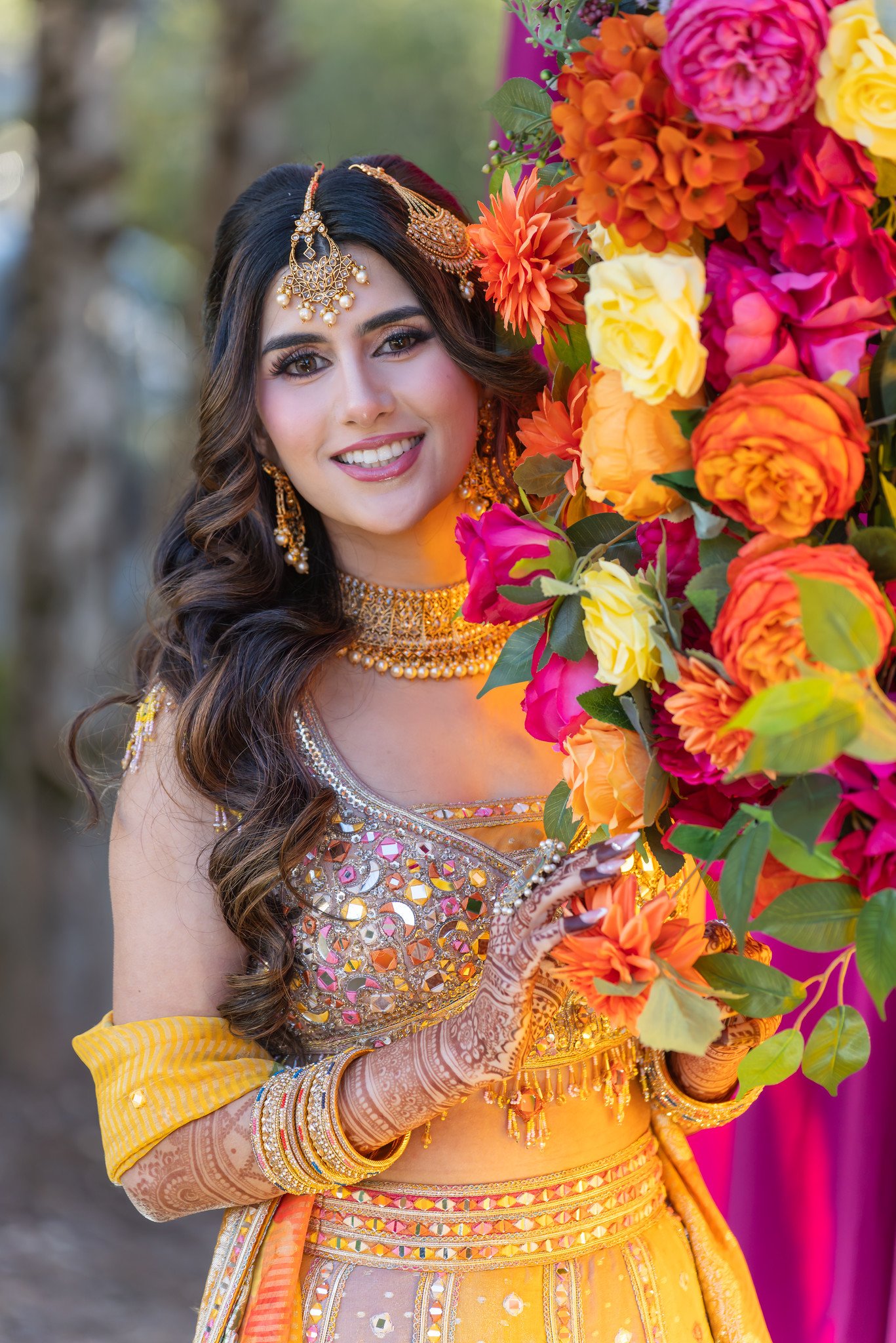 Bride smiles beside a column of pink, yellow and orange flowers.