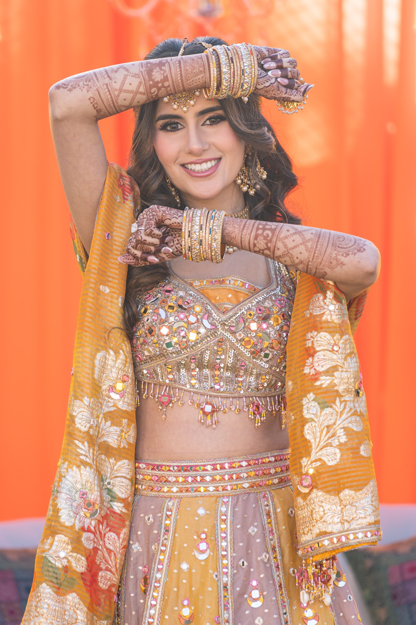 Bride smiles between her henna-decorated arms and gold bangles.