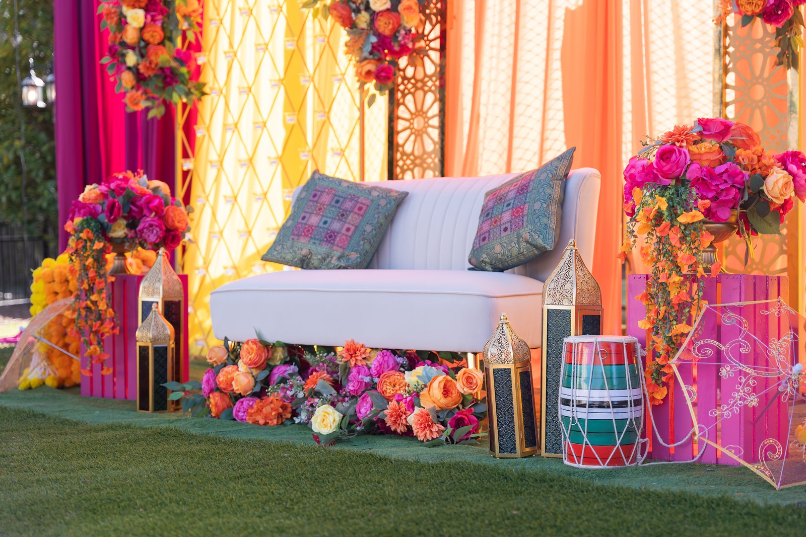 White loveseat framed by pink and orange flowers, gold lanterns and colorful drapery.