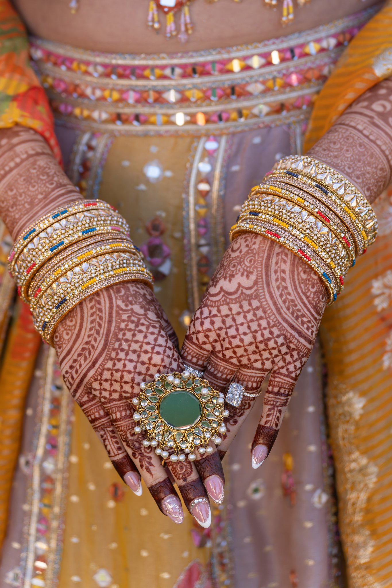 Close view of henna patterns, gold bangles and rings against an embroidered outfit.