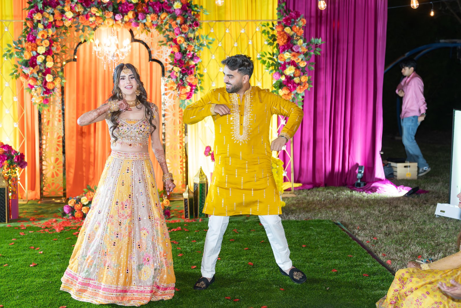 A couple dances together in front of yellow, orange and pink floral draping.