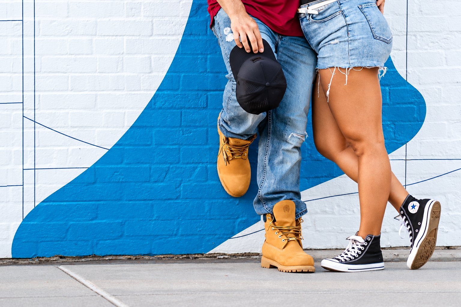 Ashley and Hunter standing close together in front of a blue and white mural