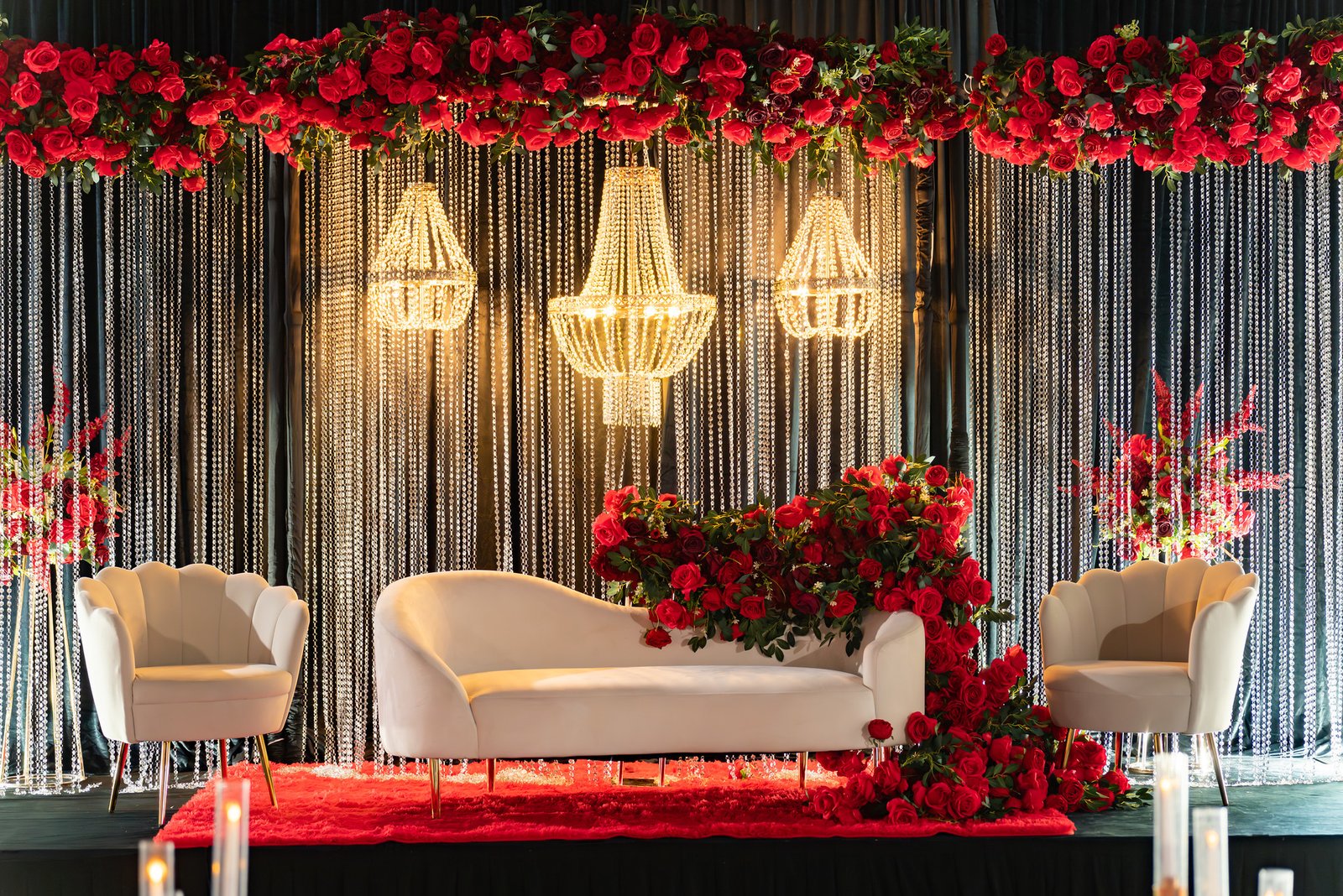 Red flowers and glowing chandeliers frame the reception seating