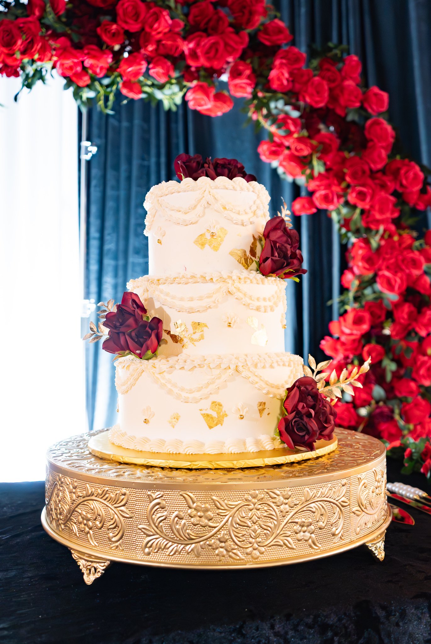 White wedding cake framed by deep red flowers