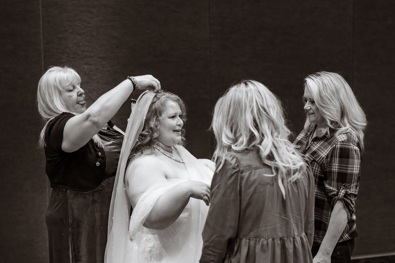 Black-and-white photograph of friends adjusting the bridal veil