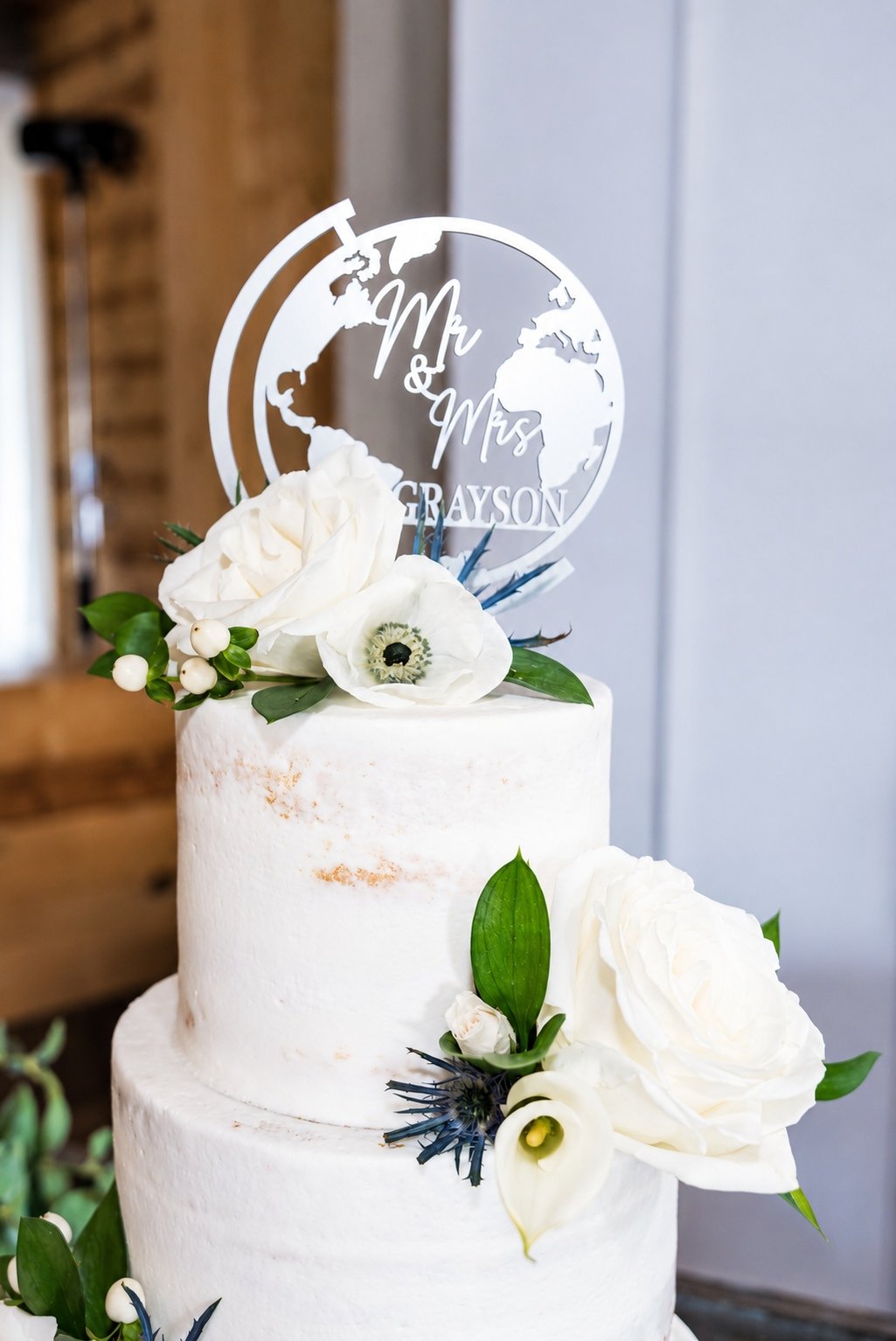 White wedding cake decorated with flowers and a personalized topper