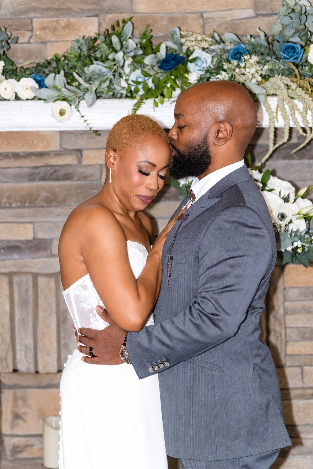 Maurice kissing Jillian’s forehead beside the ceremony flowers