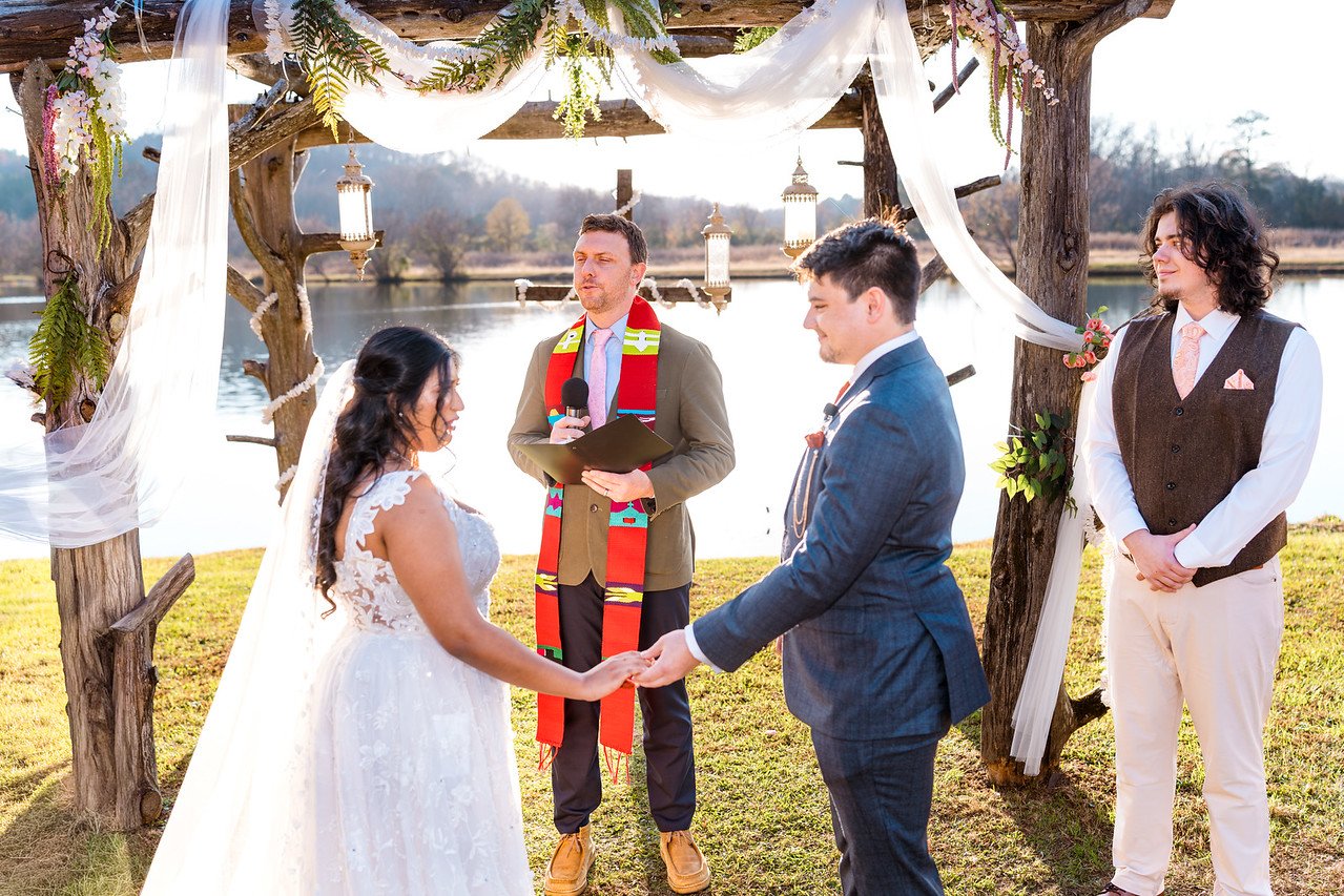 Reeham and Logan face each other beneath the ceremony arbor
